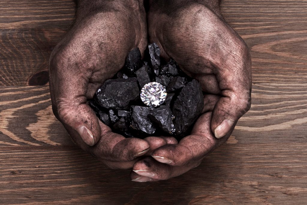 This photo shows a miner's hands holding a solitaire natural diamond amongst pieces of coal.
